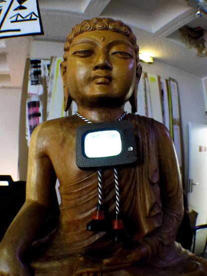 The Buddha statue in situation in the lounge at Videoformes 2017, wearing our VintageTV Bolotie consisting of a jewel integrating a small video screen, cords and cord endings shaped as cathode ray tubes displaying a single line.