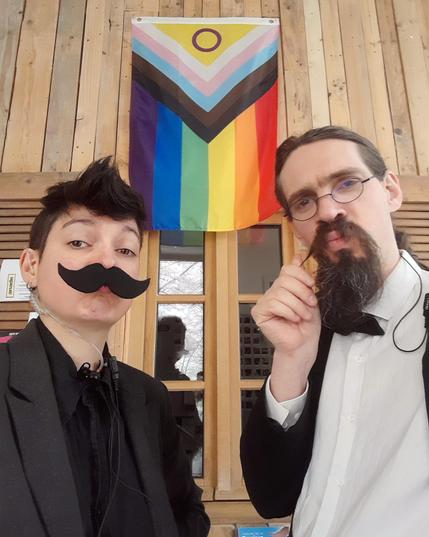 2 moustachus devant le drapeau LGBTQIA+
