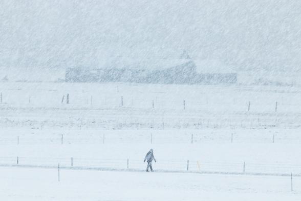 A person walking inthe Icelandic countryside in a snowstorm.