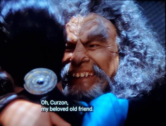 Deep Space Nine scene in three pictures. 
In pic one and two, Jadzia Dax and a old Klingon named Kor are reuniting/hugging it out. Both look absolutely thrilled to see each other. In pic three, the hug ends and they remain close. Kor is an older Klingon, white & grey scraggly  flowy hair and goatee, sharpe teeth, and forehead ridge loaf. Dax is in her blue science uniform on DS9 station. She has what looks like tattoos running up her neck on each side of her face through to the hairline. Closed caption as follows;
Pic one, focused on Kor, "Oh Curzon, my beloved old friend."
Pic two, showing Dax mid-hug, smiling big, "I'm Jadzia now."
Pic three showing both & each smiling towards one another. Kor, "Oh well, Jadzea, my beloved old friend."