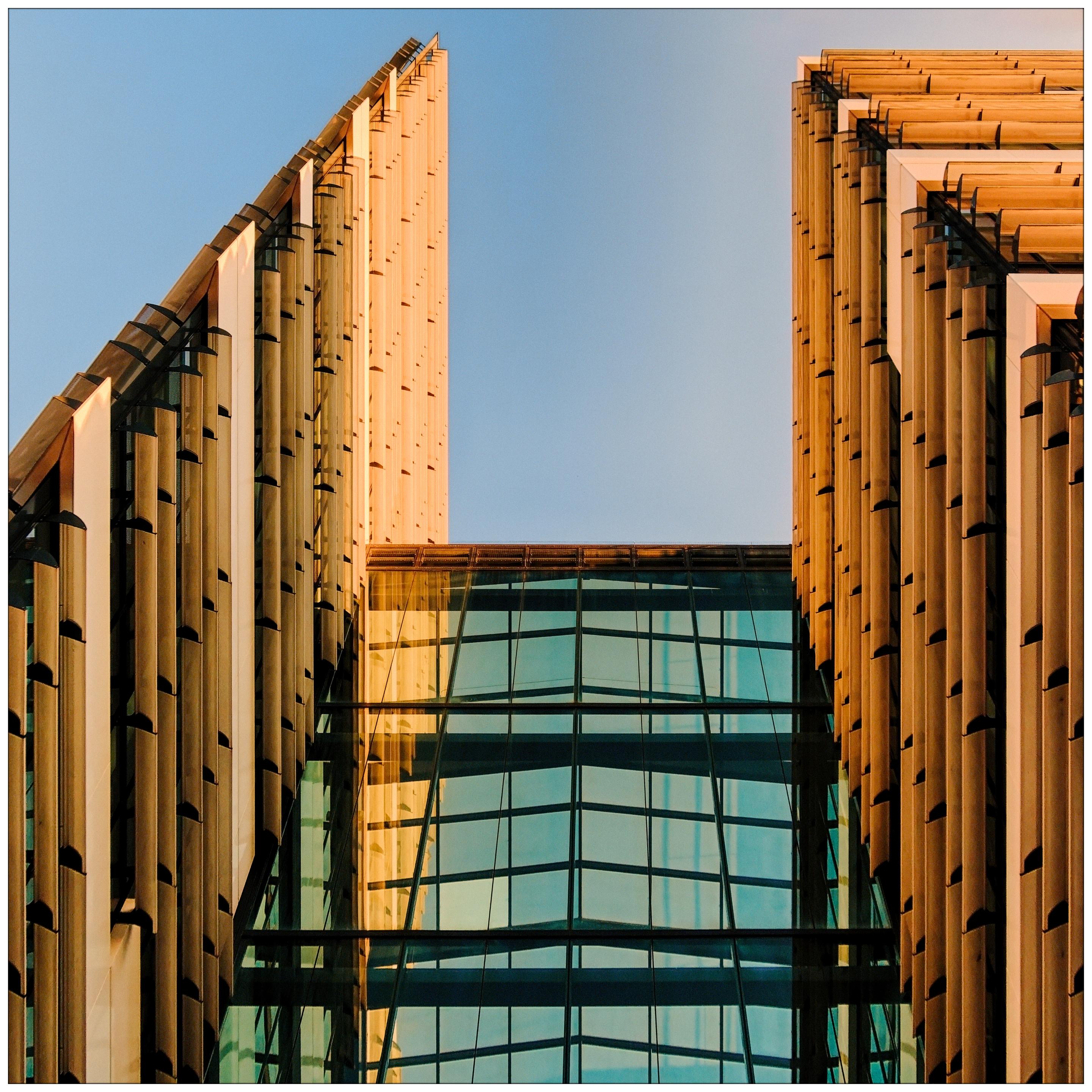Frog-perspective view of an architectural detail with bluish-green glass and creme-colored blinds against a blue sky Frog-perspective view of an architectural detail with bluish-green glass and creme-colored blinds against a blue sky