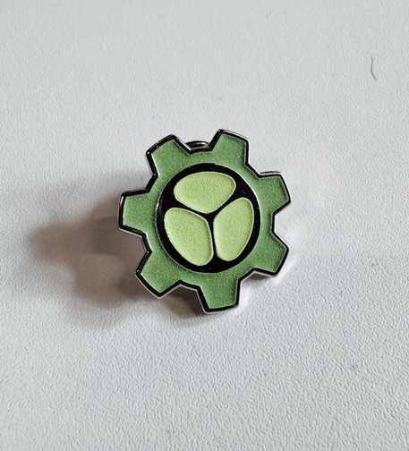 A metal pin with the Pkl logo