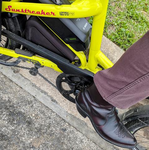 A photo of my right foot on the pedal of a 

yellow Tern HSD cargo bike with its name, Sunstreaker, in red on the seat stay

I'm wearing

wine colored western boots under a brown denim pantleg.