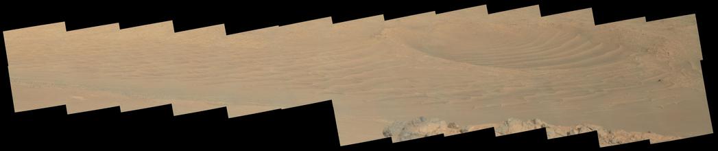 An ochre toned mosaic capturing a Martian landscape of outcrops and dunes. The right hand side of the mosaic captures a dune-filled impact crater.