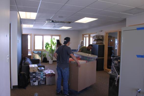 A photo of the new Aftersight office with moving happening. Two men roll a large box full of smaller boxes. 