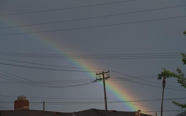 Even close zoom of end of the of the rainbow rising above a rooftop, crisscrossed by utility lines