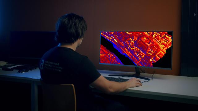 Symbolbild Fernerkundung 3D Thermographie zeigt Person am Bildschirm mit rot-gelben Wärmebildaufnahmen einer Stadt