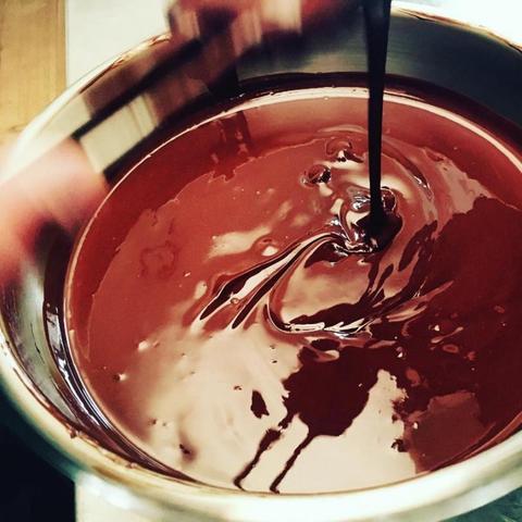 Foto af en stålskål fyldt med smeltet, mørk chokolade.