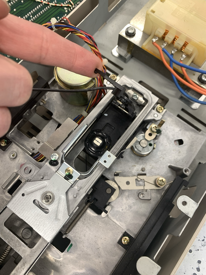 Innenansicht eines Commodore 1541 Diskettenlaufwerks; ein Finger zeigt auf den Schreib-/Lesekopf, zur Diagnose eines ‚?FILE NOT FOUND‘-Fehlers.