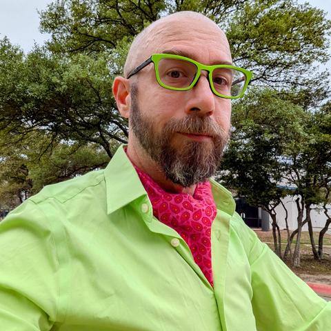 A photo of me, a 47 year old white man with a shaved head, a short cropped brown & grey beard, 

photographed from the chest up

In front of some live oak trees in an office park,

wearing

rectangular lime green acetate glasses, a bright magenta ascot under a lime green dress shirt