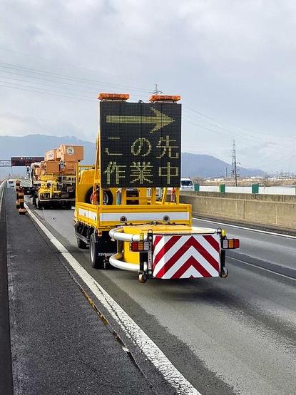 2 large trucks on the side of a highway in Japan. The truck in the foreground is yellow with an illuminated message board on the back with a Scorpion II Metro Slim crash attenuator mounted below. The Metro Slim version of our Scorpion II is perfect for lighter weight vehicles in high density areas.