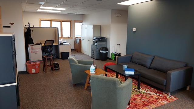 photo post move. A rug and comfy furniture have been put in place. A large brailler, printer, and cabinets have also been placed in frame. Feels homier but there is still mess there is no art hung on the walls. 