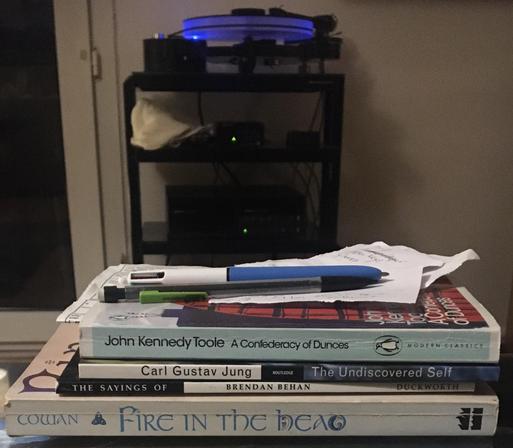 the books are piled in the foreground with a pen and notes on top; in the background a record is playing on a record player 