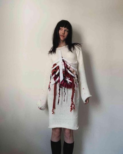 Woman wearing a crocheted sweater dress with a crocheted, anatomical torso design featuring red and white yarn.