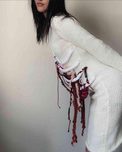 Woman wearing a white crochet sweater with colorful yarn threads creating a stylized, visceral representation of internal organs.