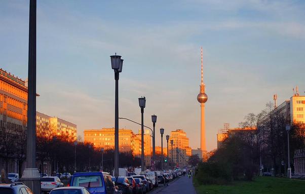 Berli, Blick entlang der Karl-Marx-Allee Richtung Westen. Im Hintergrund der Fernsehturm. Die Häuser werden im oberen Drittel von der Morgensonne beschienen und leuchten orange. 