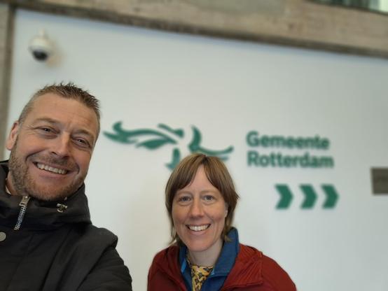 Foto met twee personen bij het logo van de gemeente Rotterdam