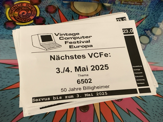 Flyer für das Vintage Computer Festival Europa 2025 auf einem bunten Flipper-Automaten. Darauf angekündigt: VCFe am 3./4. Mai 2025 in München, Thema 6502, 50 Jahre Billigheimer