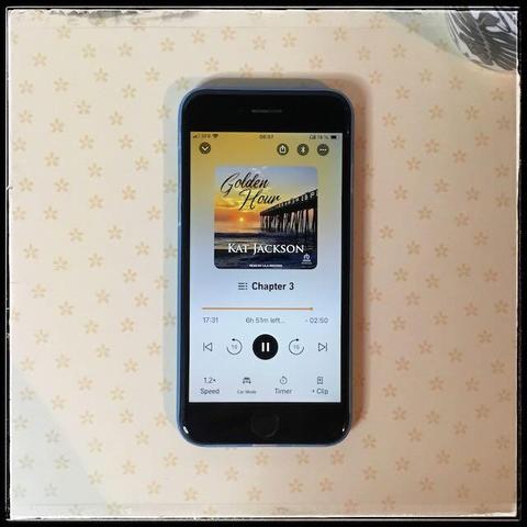 On a sunny background, an iPhone with the cover of Golden Hour by Kat Jackson, narrated by Lila Winters.
