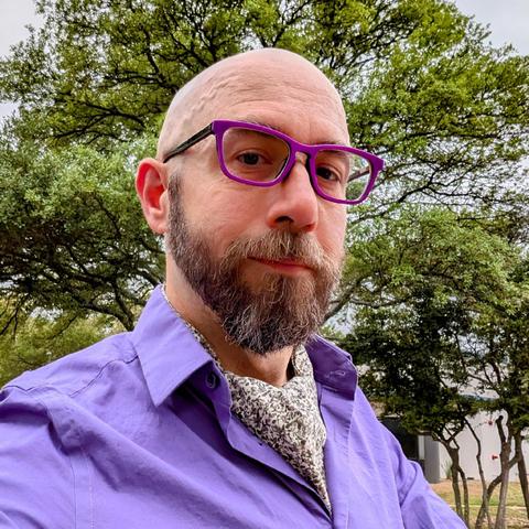 A photo of me, a 47 year old white man with a shaved head, a short cropped brown & grey beard, 

photographed from the chest up

In front of some live oak trees in an office park,

wearing

rectangular purple acetate glasses, a grey floral ascot under a purple dress shirt