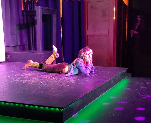 Another photo of Austin Tacious, this time lying on the ground, kicking his feet (which are in cowboy boots, of course), and propping his head up on both hands.