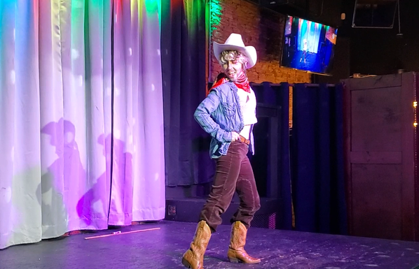 Another photo of Austin Tacious, this time wearing a white cowboy hat in addition to the costume, and dancing with his hands on his hips.