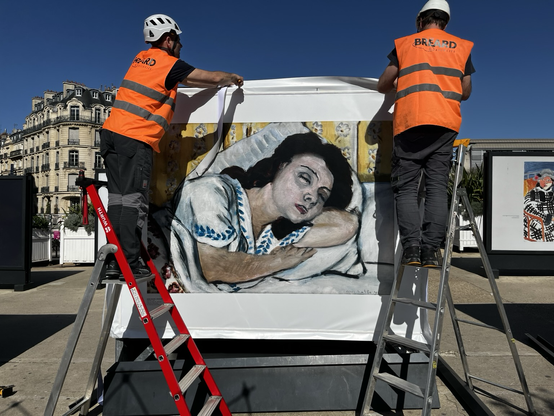 Deux techniciens installent un grand format représentant une femme assoupie 