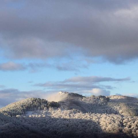 
Una vista panorámica de una cordillera cubierta de nieve bajo un cielo parcialmente nublado. La nieve cubre los árboles y las colinas, creando un paisaje invernal sereno. El cielo es una mezcla de azul claro y nubes grises, con una iluminación suave que sugiere la hora del amanecer o el atardecer. La escena transmite una sensación de tranquilidad y belleza natural.