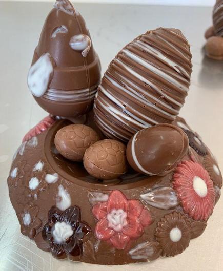 Das Foto zeigt ein Osternest aus Schokolade. Das Nest ist mit bunten Schokoladenblüten verziehrt und mit einem Schoko-Huhn und verschiedenen Schokoladeneiern gefüllt.