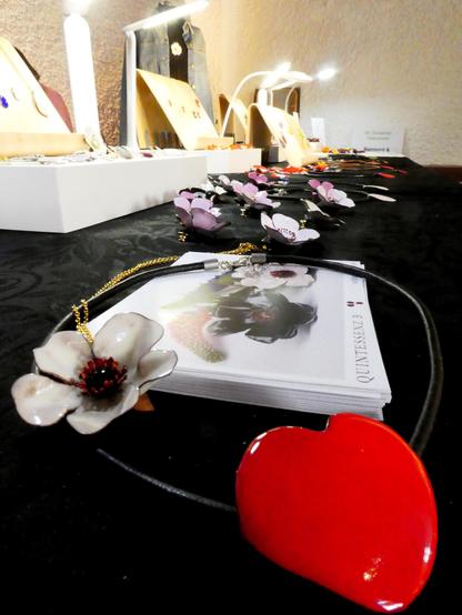 Le stand Quintessenz B avec une multitude de bijoux floraux colorés. Au premier plan une rose blanche et un pétale de rose rouge en forme de cœur.