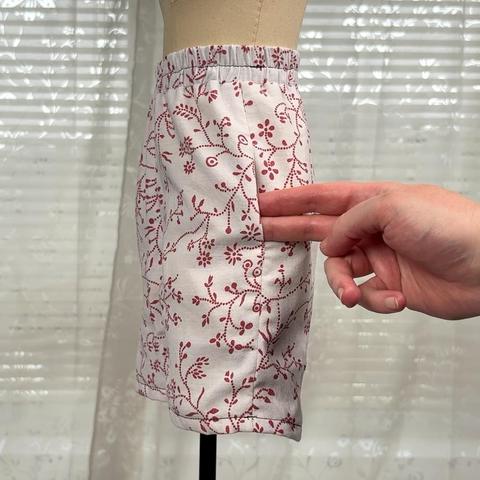 White Boxershorts with red floral pattern on a half scale dressform. A hand is showing where the pockets sit.