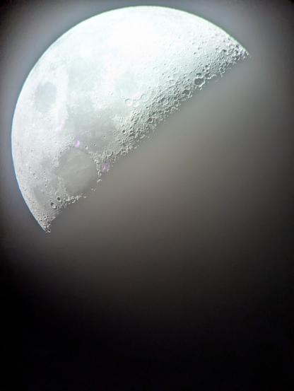Der halb beleuchtete Mond durchs Teleskop. An der Tag-Nacht-Grenze sind klar die Krater zu erkennen.