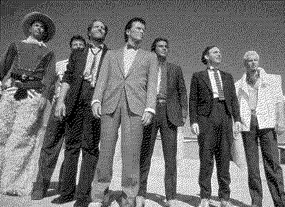seven dudes stand against an empty sky shot from a very low angle. it is team banzai from the movie buckaroo banzai.