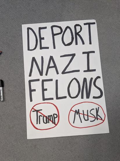 Handwritten sign that reads DEPORT NAZI FELONS in black text. At the bottom reads Trump, crossed out in red sharpie, Musk also crossed out in red sharpie.