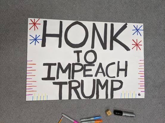 Back of the second sign that reads HONK TO IMPEACH TRUMP in black sharpie. 