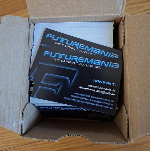 Das Foto zeigt eine kleine Pappbox gefüllt mit Visitenkarten im Futuremania-Design: Schwarzer Hintergrund, blauer "Futuremania"-Schriftzug, links das leuchtende "F" und rechts die Kontaktdaten in blau und weiß...