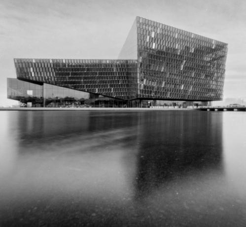 The concert hall Harpa in Reykjavik. Black and white picture taken with a pinhole film camera. In the foreground is a reflection of the building in the manmade pool in front of the building.