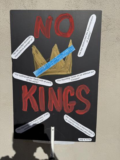Black Sign saying “No Kings” with gold crown and a blue line over it.