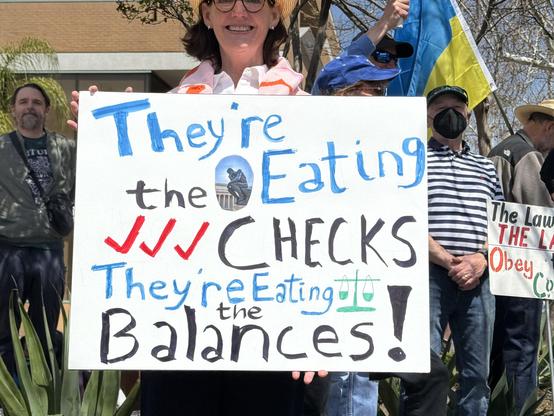 Sign saying “They’re eating the Checks they’re eating the Balances!”