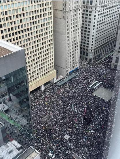Daley Plaza and W Washington Street in Chicago, seen from above, completely swarmed with people marching in opposition to Trump, Musk, Project 2025, and against other right wing nonsense.