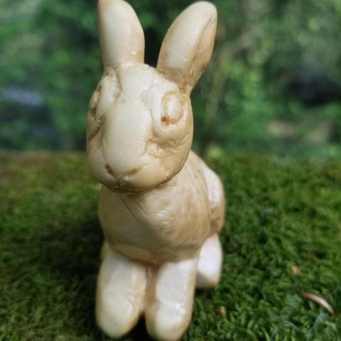 a small carved jackrabbit, sitting on its haunches, on a mossy railing in the woods.