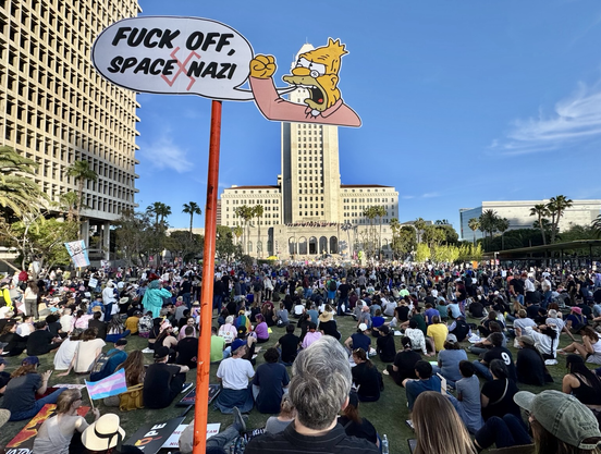 Photo of the crowds gathered in front of the LA city hall, thousands of them. I’m holding my sign in front of the tall building, one of the  “Old man yells at cloud” Simpsons meme that has him say “Fuck off, space Nazi!”