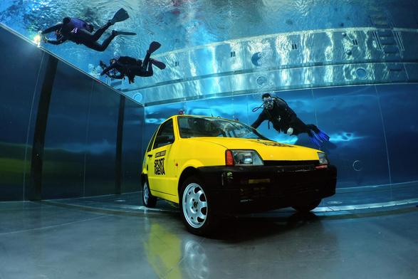 A yellow car in a pool with divers around it 