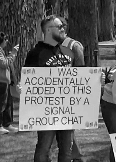Black-and-White photo of a white dude with short hair, glasses and beard holding a large protest sign "I was accidentally added to this protest by a signal group chat".

The corners of the sign are decorated with the emojis "oncoming fist", "flag: United States" and "fire" (like used in the legendary leaked Signal Chat "Houthi PC small group" by Michael Waltz)