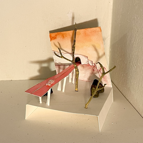 A small scale sculpture made of paper, with a bridge going toward a wall and through a tunnel, over trees and rocks. A car is on that pink road.