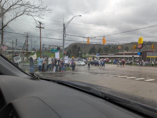 A large crowd of people standing on the corners of an intersection holding signs in protest of the Trump administration.
