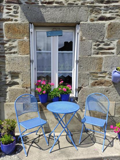 Deux chaises bleues patientent devant une maison au mur blanc.
Une table assortie attend le café de 15h, ou rien du tout.
Un panneau discret annonce : "Je suis à la retraite".
Les géraniums sourient, et le vent ne fait aucun commentaire