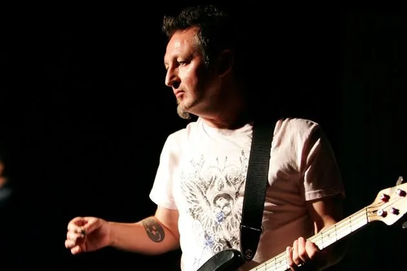 photo of Dave Allen, holding a Music Man bass guitar. 