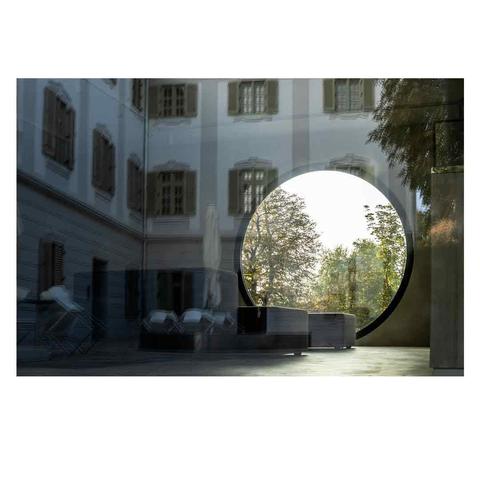 The picture was taken through a large glass window. The café opposite has a round glass window through which we can see trees. The glass in the foreground reflects the other wing of the Baroque castle.