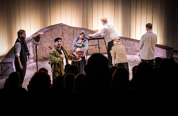 Five people standing on stage playing different roles in a theatre performance
